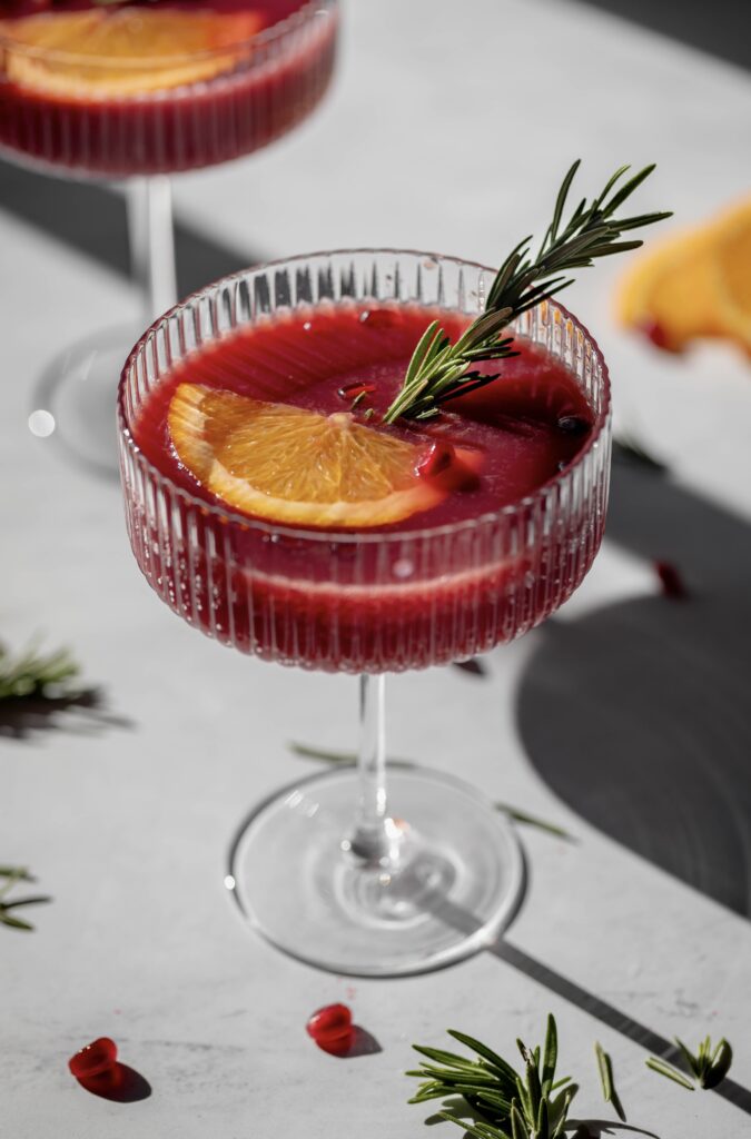 glass of sparkling pomegranate citrus mocktail with an orange slice and rosemary sprig as garnish