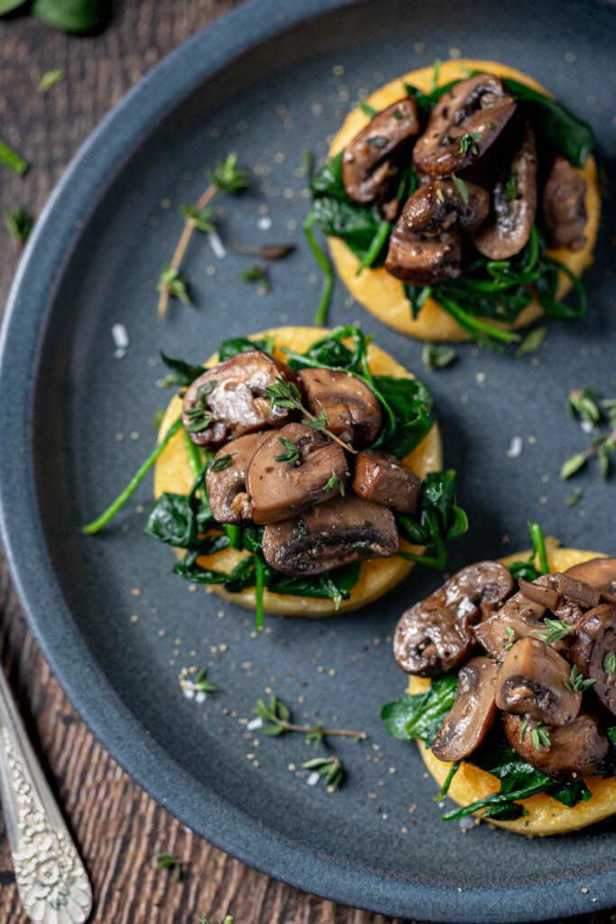 polenta rounds on a plate with spinach and mushrooms on top